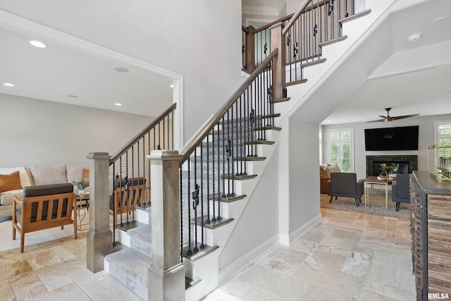 6531 Eagle Ridge Rd, Bettendorf, IA 52722 - stairway with stone tile flooring, a ceiling fan, a glass covered fireplace, a high ceiling, and baseboards