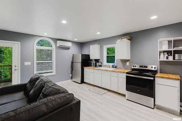 kitchen featuring appliances with stainless steel finishes, butcher block counters, a wall mounted air conditioner, light wood-style floors, and white cabinetry