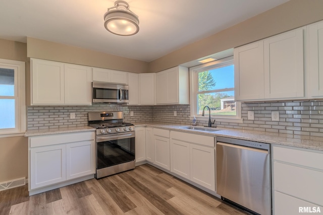 8501 49th St, Coal Valley, IL 61240 - kitchen with appliances with stainless steel finishes, a sink, white cabinets, decorative backsplash, and light wood-type flooring