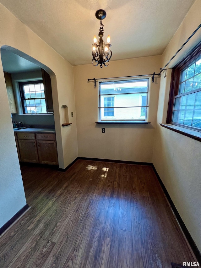 3752 12th St, Rock Island, IL 61201 - unfurnished dining area featuring arched walkways, dark wood finished floors, a chandelier, and healthy amount of natural light