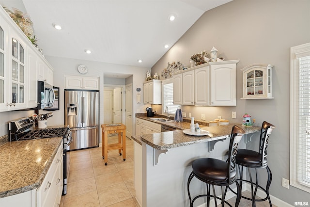 1361 Pinnacle Pines Ct, Bettendorf, IA 52722 - kitchen with appliances with stainless steel finishes, vaulted ceiling, a kitchen bar, a peninsula, and glass insert cabinets