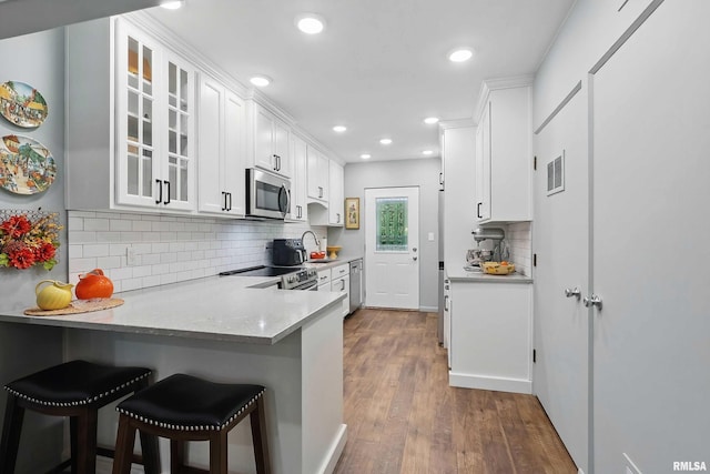 1104 Kimberly Rd Unit 1006, Bettendorf, IA 52722 - kitchen with appliances with stainless steel finishes, glass insert cabinets, white cabinets, a kitchen breakfast bar, and backsplash