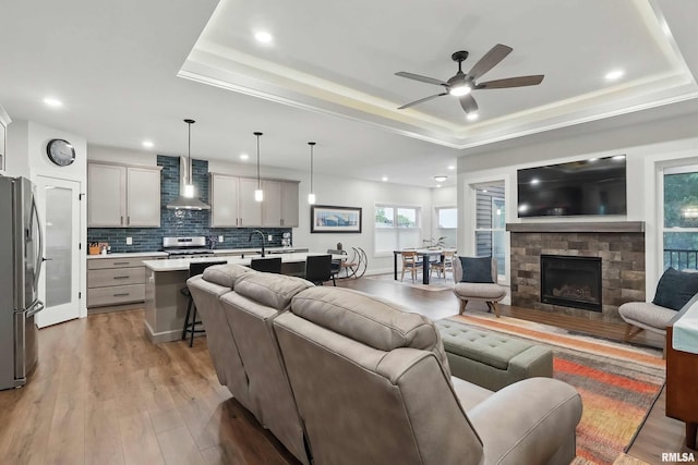 1327 Heights Ct, Bettendorf, IA 52803 - living room with a tray ceiling, ceiling fan, light wood-style floors, a stone fireplace, and recessed lighting