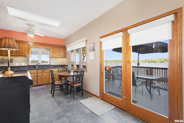 22867 Great River Rd, Le Claire, IA 52753 - kitchen featuring brown cabinetry, a ceiling fan, decorative backsplash, dark countertops, and a sink