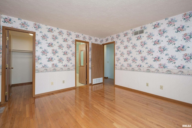 4675 Kynnelworth Dr Unit 301, Bettendorf, IA 52722 - unfurnished bedroom with wallpapered walls, light wood finished floors, a spacious closet, baseboards, and a textured ceiling