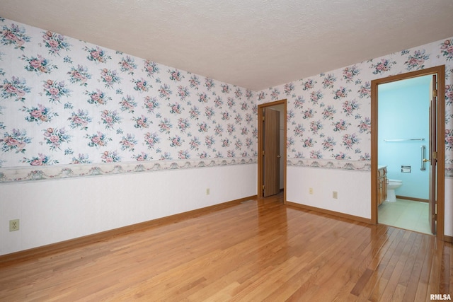4675 Kynnelworth Dr Unit 301, Bettendorf, IA 52722 - unfurnished room with light wood-style flooring, wallpapered walls, a textured ceiling, and baseboards