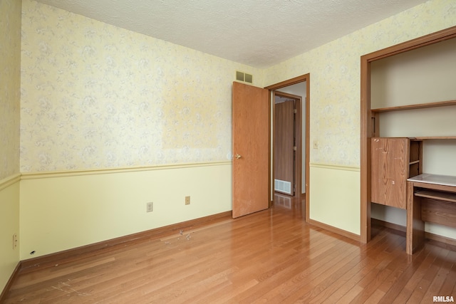 4675 Kynnelworth Dr Unit 301, Bettendorf, IA 52722 - unfurnished bedroom with wallpapered walls, hardwood / wood-style flooring, a textured ceiling, wainscoting, and baseboards