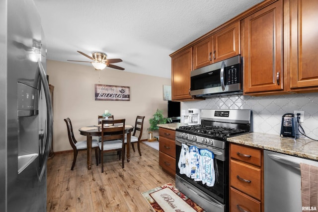 2614 W 59th St, Davenport, IA 52806 - kitchen with stainless steel appliances, brown cabinetry, ceiling fan, light wood-style floors, and light stone countertops