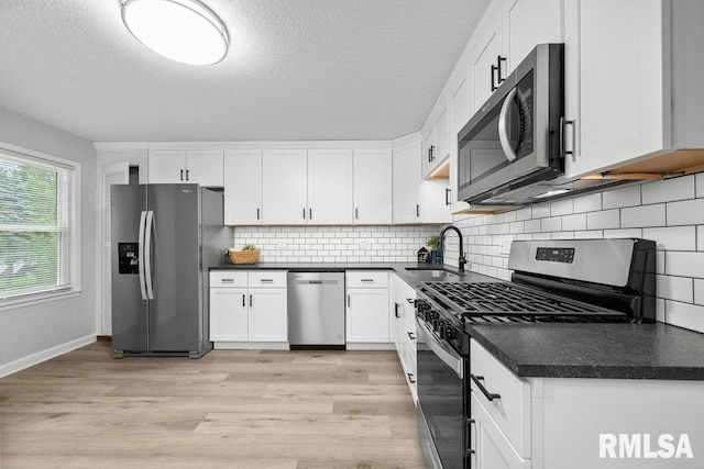 1156 23rd St, Moline, IL 61265 - kitchen featuring stainless steel appliances, dark countertops, white cabinets, light wood finished floors, and a textured ceiling