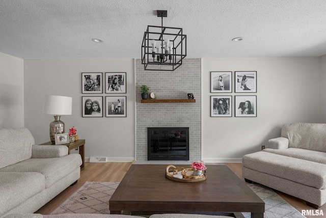 28013 230th St, Le Claire, IA 52753 - living room with wood finished floors, a textured ceiling, a brick fireplace, baseboards, and a chandelier