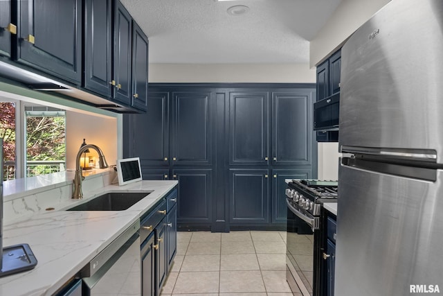 28013 230th St, Le Claire, IA 52753 - kitchen with stainless steel appliances, a sink, blue cabinetry, light stone countertops, and light tile patterned floors