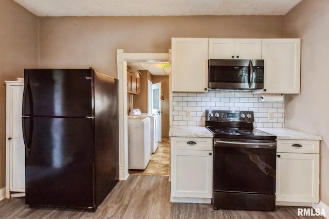 417 12th St, De Witt, IA 52742 - kitchen with black appliances, washer and clothes dryer, light wood-type flooring, white cabinetry, and tasteful backsplash