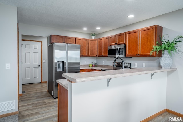 4260 Sapphire Ln, Bettendorf, IA 52722 - kitchen with appliances with stainless steel finishes, a peninsula, brown cabinetry, light wood-style floors, and light countertops