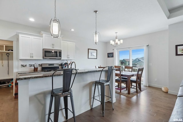 4241 Colorado Dr, Bettendorf, IA 52722 - kitchen with stainless steel appliances, dark wood-type flooring, a breakfast bar, white cabinetry, and a chandelier