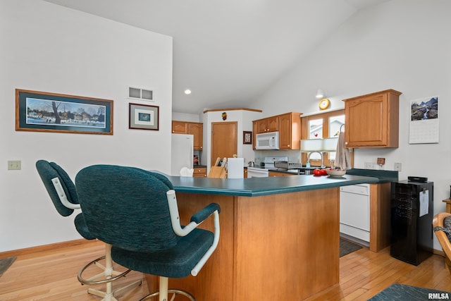 5142 Fillmore Ct, Davenport, IA 52806 - kitchen with white appliances, vaulted ceiling, dark countertops, light wood finished floors, and a breakfast bar