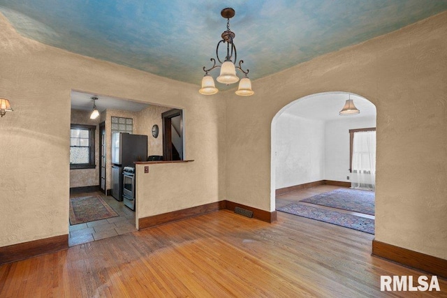 2446 16th Ave, Moline, IL 61265 - unfurnished dining area featuring arched walkways, wood finished floors, a textured wall, a chandelier, and baseboards