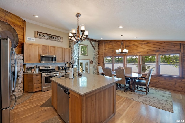 905 1st St, Camanche, IA 52730 - kitchen with stainless steel appliances, a chandelier, vaulted ceiling, wooden walls, and a textured ceiling