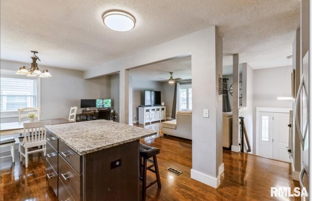 3071 S Hampton Dr, Bettendorf, IA 52722 - kitchen featuring a breakfast bar area, dark brown cabinetry, a textured ceiling, dark wood-style floors, and a ceiling fan