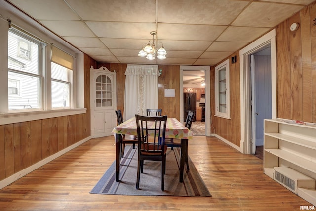 627 5th Ave S, Clinton, IA 52732 - dining space with light wood-style flooring, wood walls, a chandelier, baseboards, and a drop ceiling