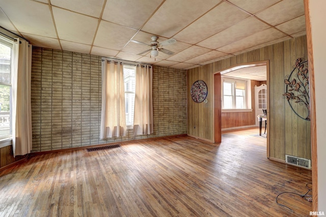 627 5th Ave S, Clinton, IA 52732 - empty room with hardwood / wood-style floors, ceiling fan, brick wall, wood walls, and a drop ceiling