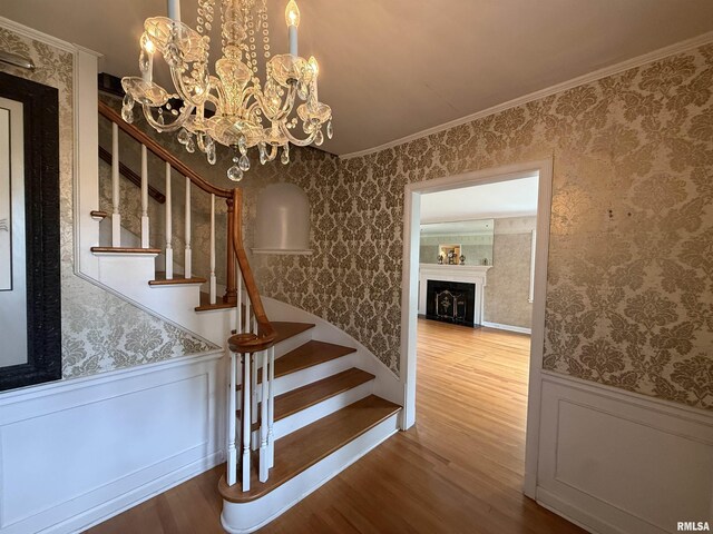 215 3rd St, Carmi, IL 62821 - staircase with wood finished floors, wainscoting, ornamental molding, wallpapered walls, and a chandelier