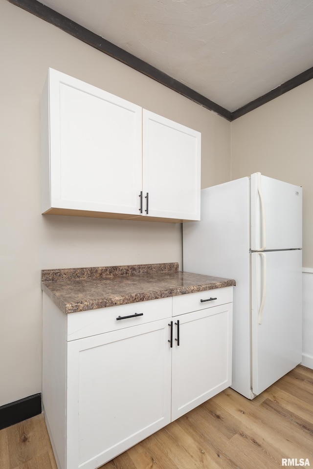 1522 Bridge Ave, Davenport, IA 52803 - kitchen with dark countertops, white cabinetry, light wood-style floors, freestanding refrigerator, and ornamental molding