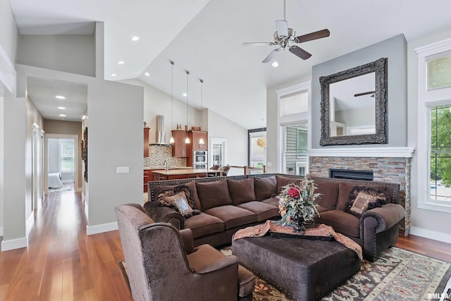 7 Redstone Ct, Le Claire, IA 52753 - living area with lofted ceiling, light wood finished floors, a stone fireplace, a ceiling fan, and baseboards