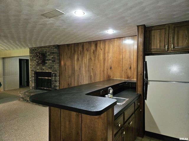 2120 Fareway Dr, Muscatine, IA 52761 - kitchen featuring freestanding refrigerator, a sink, dark countertops, a textured ceiling, and a brick fireplace