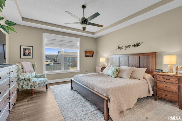 6997 Matthews Pass, Bettendorf, IA 52722 - bedroom with wood finished floors, a tray ceiling, baseboards, ceiling fan, and a textured ceiling