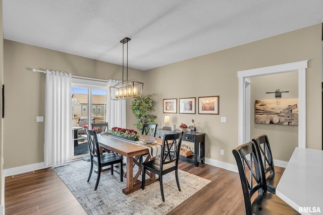 6997 Matthews Pass, Bettendorf, IA 52722 - dining area featuring a chandelier, dark wood-style flooring, baseboards, and a textured ceiling