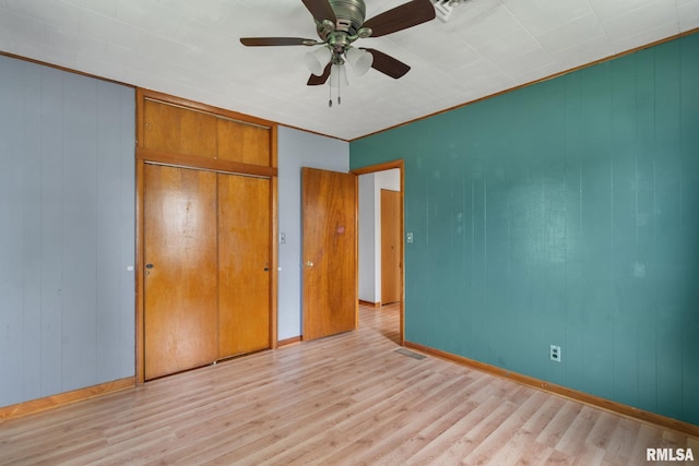 1323 113th Ave, Milan, IL 61264 - unfurnished bedroom with light wood finished floors, a closet, a ceiling fan, baseboards, and wooden walls