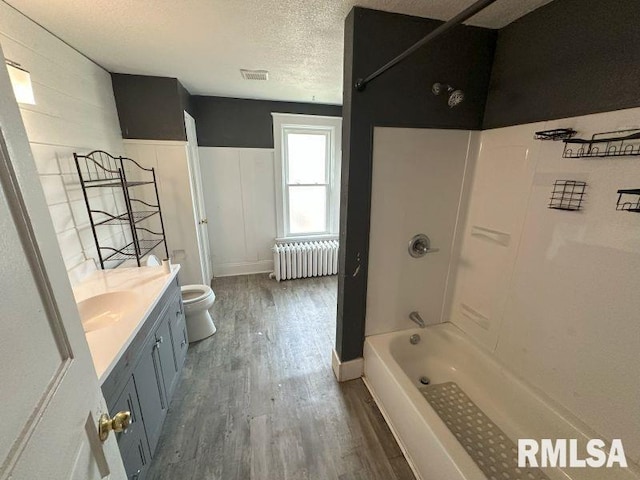317 9th St, De Witt, IA 52742 - full bath featuring radiator heating unit, wood finished floors, toilet, vanity, and tub / shower combination