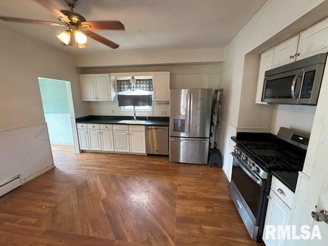 317 9th St, De Witt, IA 52742 - kitchen featuring appliances with stainless steel finishes, a sink, dark countertops, a ceiling fan, and wainscoting