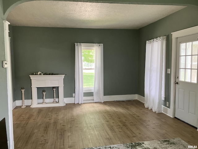 136 W Mill St, Kewanee, IL 61443 - unfurnished living room with arched walkways, wood finished floors, healthy amount of natural light, a textured ceiling, and baseboards