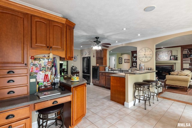 1300 W Brewster Rd, Herrin, IL 62948 - kitchen featuring freestanding refrigerator, a breakfast bar, a peninsula, a glass covered fireplace, and a ceiling fan