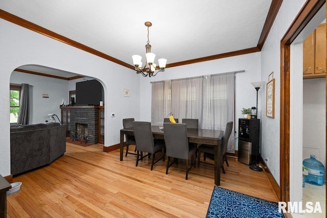 2531 5th St, Moline, IL 61265 - dining room featuring arched walkways, a chandelier, light wood-type flooring, a brick fireplace, and crown molding