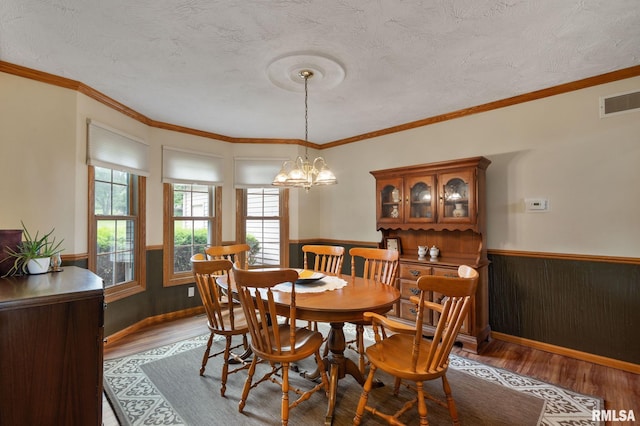 1010 Meadows Cir, Bettendorf, IA 52722 - dining room featuring wainscoting, wood finished floors, a chandelier, a textured ceiling, and ornamental molding