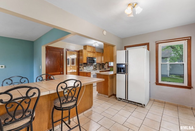 204 E Main St, Joy, IL 61260 - kitchen featuring white appliances, tile countertops, a breakfast bar area, backsplash, and light tile patterned floors