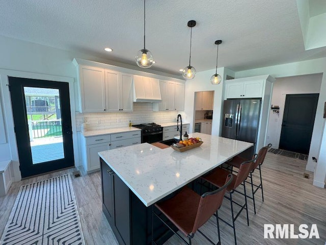 1722 17th St, De Witt, IA 52742 - kitchen with black gas stove, custom range hood, light wood-style floors, backsplash, and a textured ceiling