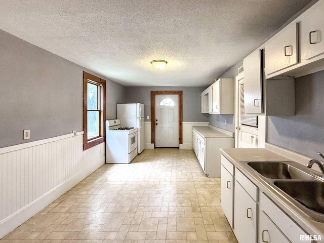 511 Fulton St, Grand Mound, IA 52751 - kitchen with white stove, light countertops, white cabinets, a textured ceiling, and a wainscoted wall