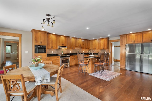 3473 270th St, De Witt, IA 52742 - kitchen featuring stainless steel appliances, under cabinet range hood, recessed lighting, dark wood-style flooring, and decorative backsplash