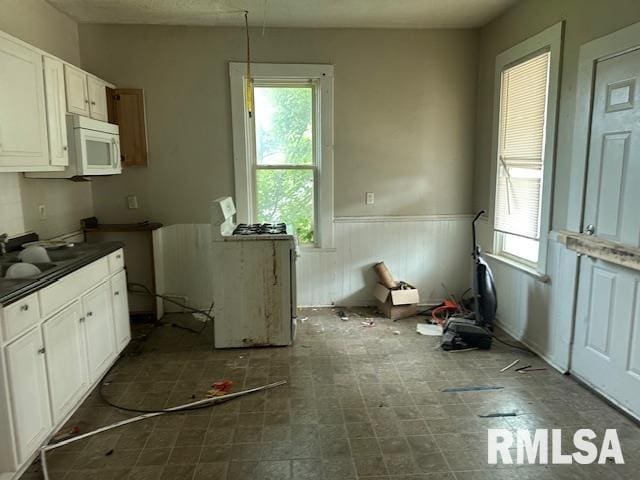 1919 Sturdevant St, Davenport, IA 52804 - kitchen with white microwave, a wainscoted wall, dark countertops, white cabinets, and dark flooring