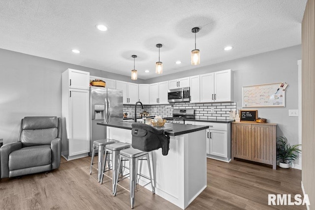 3307 Clover Hills Dr, Bettendorf, IA 52722 - kitchen featuring stainless steel appliances, dark countertops, wood finished floors, decorative backsplash, and white cabinetry