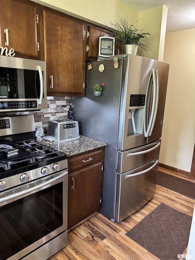 101 E 6th St, Sherrard, IL 61281 - kitchen featuring appliances with stainless steel finishes, light wood finished floors, dark brown cabinets, and stone countertops
