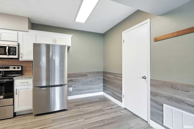 3045 4th St Unit 1, Moline, IL 61265 - kitchen with stainless steel appliances, white cabinetry, light wood-type flooring, a wainscoted wall, and light stone counters
