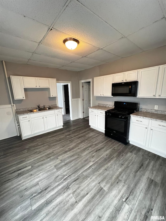 201 N 20th St, East Moline, IL 61244 - kitchen with black appliances, a drop ceiling, white cabinetry, wainscoting, and dark wood finished floors
