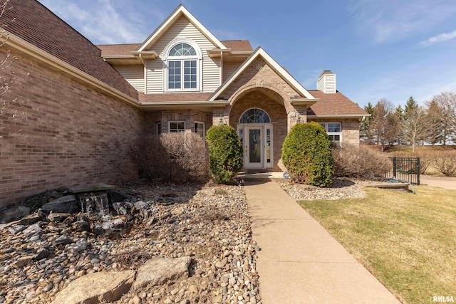 4934 Foxborough Ct, Bettendorf, IA 52722 - property entrance featuring brick siding, a yard, a shingled roof, and a chimney