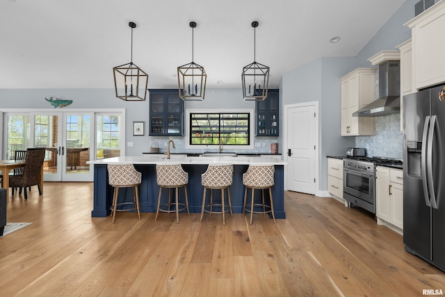 223 N 2nd St, Le Claire, IA 52753 - kitchen featuring appliances with stainless steel finishes, wall chimney exhaust hood, backsplash, glass insert cabinets, and vaulted ceiling