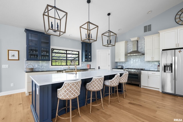 223 N 2nd St, Le Claire, IA 52753 - kitchen with appliances with stainless steel finishes, wall chimney exhaust hood, a kitchen island with sink, light wood-type flooring, and backsplash