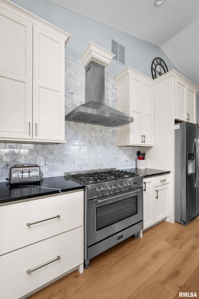 223 N 2nd St, Le Claire, IA 52753 - kitchen featuring stainless steel appliances, wall chimney range hood, light wood-style flooring, vaulted ceiling, and dark countertops